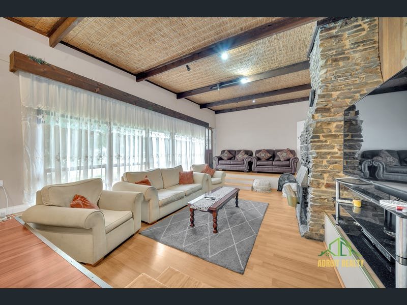 Spacious sunken living room featuring a large stone fireplace, exposed timber ceiling beams with woven textures, and light wood-look flooring.