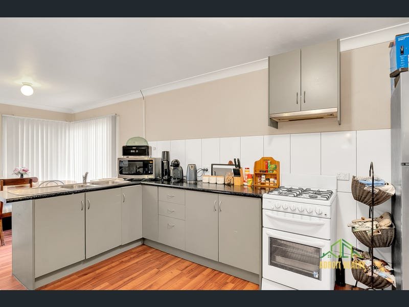 Interior view of a functional kitchen featuring an L-shaped counter, integrated double sink, white tiled backsplash, and various countertop appliances.
