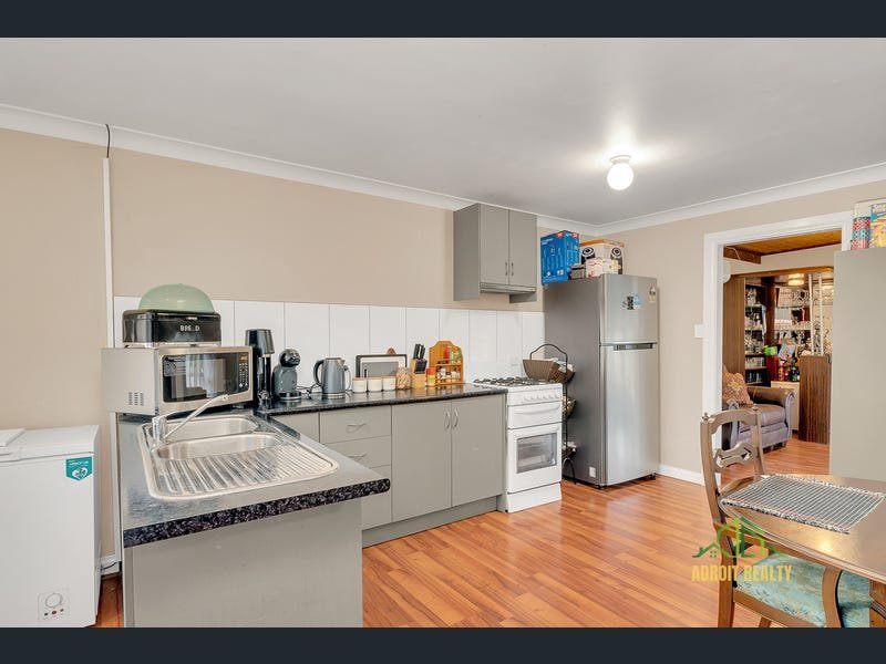 Interior view of a functional kitchen with a double sink, black countertops, white tiled backsplash, and an adjacent dining area.