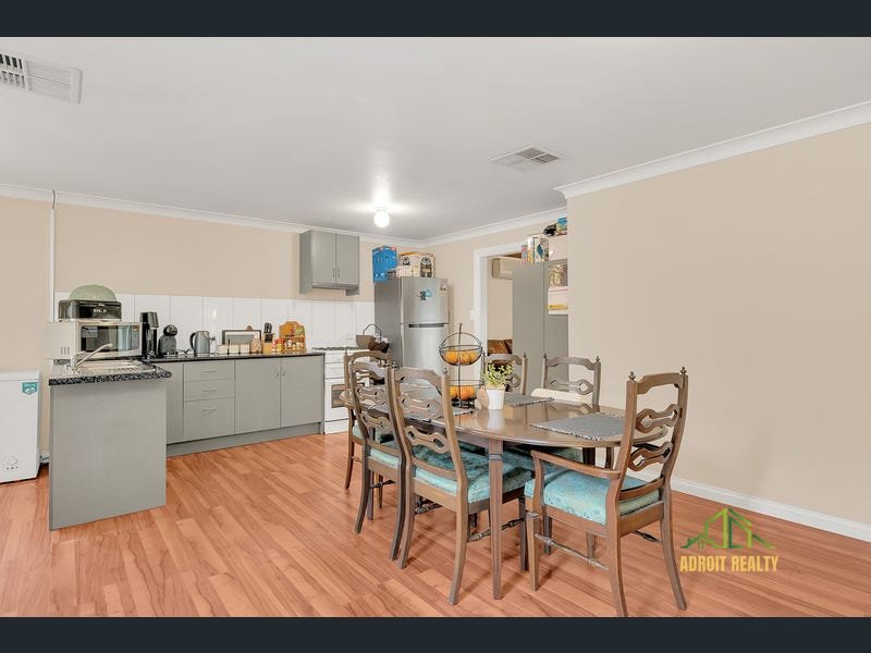 Open-plan kitchen and dining area featuring grey cabinetry, a stainless steel refrigerator, and a wooden dining set on laminate flooring.