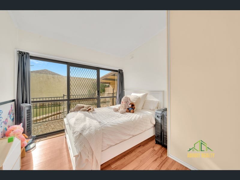 Bright bedroom with a white bed frame, plush bedding, and large sliding glass doors leading to a fenced outdoor area.