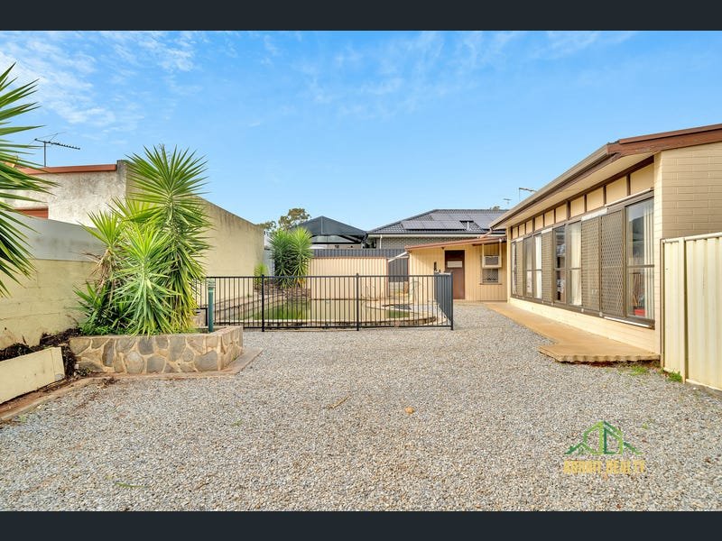 Outdoor view of a residential property featuring a large gravel area, a metal security fence around a pool, and the rear exterior of a tan house.