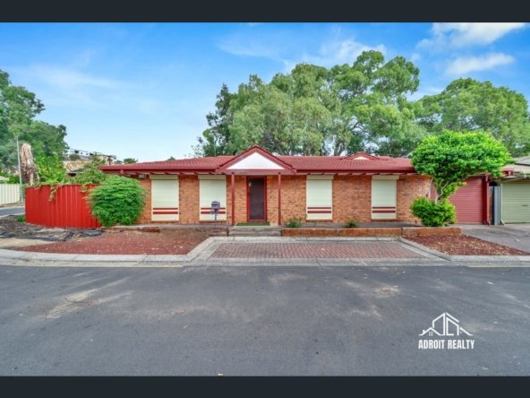 Red brick single-story home with a tiled roof, featuring cream roller shutters on front windows and a paved driveway.
