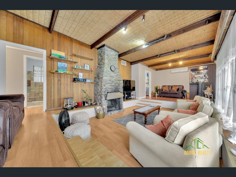 Interior view of a multi-level lounge area with light wood flooring, neutral-toned sofas, and a built-in bar area in the background.