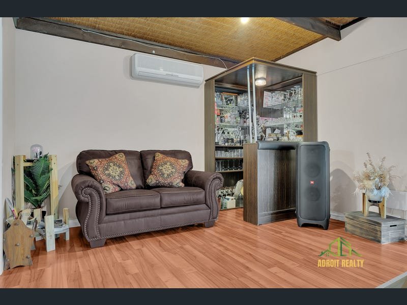 Modern home entertainment corner featuring a brown leather loveseat, polished wood-look flooring, a wall-mounted air conditioner, and a built-in bar cabinet with glassware.